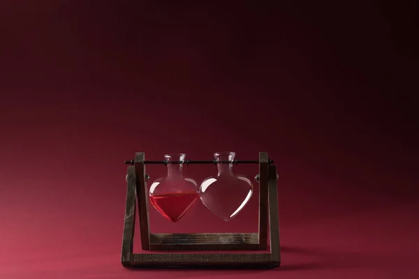 Стеклянная банка в форме сердца с духами и пустой стеклянный кувшин на деревянный стенд на красный — стоковое фото