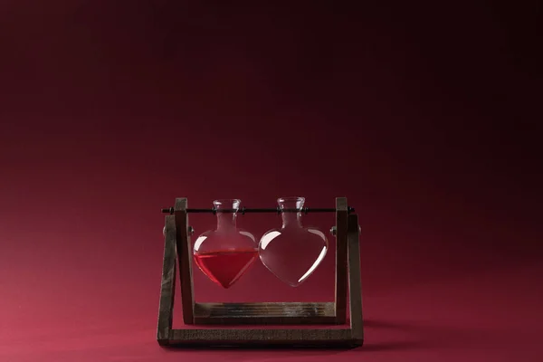 Heart shaped glass jar with perfume and empty glass jar on wooden stand on red — Stock Photo