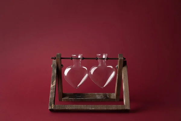Two empty heart shaped glass jars on wooden stand on red — Stock Photo