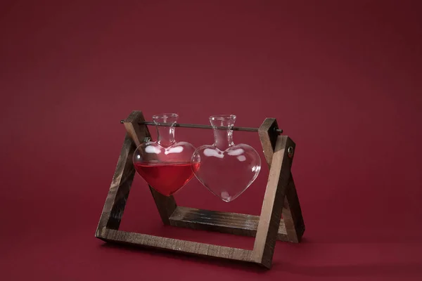 Pot en verre en forme de coeur avec parfum et pot en verre vide sur support en bois sur rouge — Photo de stock