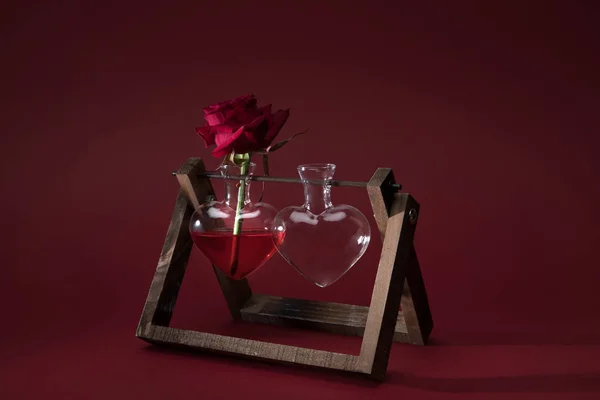 Red rose in heart shaped vase and empty vase on wooden stand on red — Stock Photo