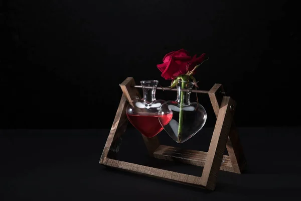 Red rose in heart shaped vase and vase with love elixir isolated on black — Stock Photo