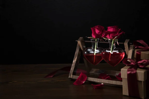 Zwei rote Rosen in herzförmigen Vasen auf Holzständern und Geschenkboxen — Stockfoto