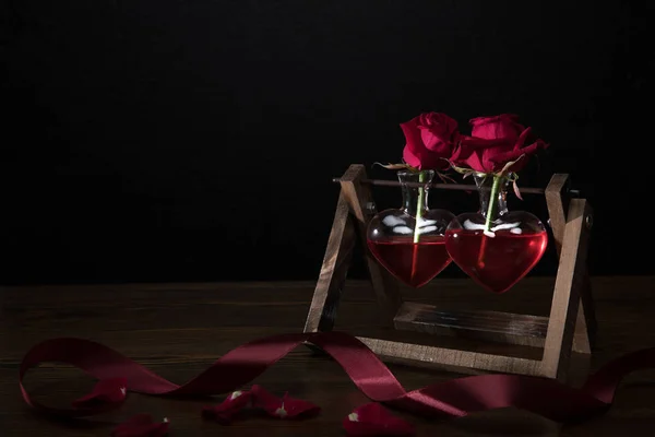 Two red roses in heart shaped vases on wooden stand — Stock Photo