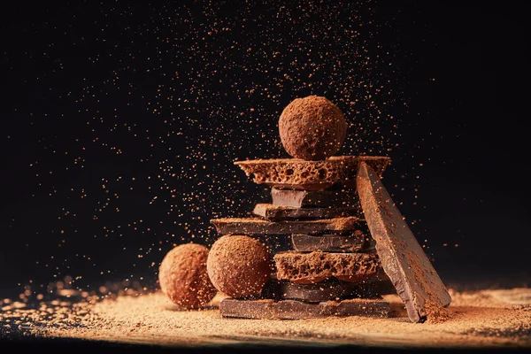 Vue rapprochée de l'arrangement des truffes et des barres de chocolat avec de la poudre de cacao sur noir — Photo de stock