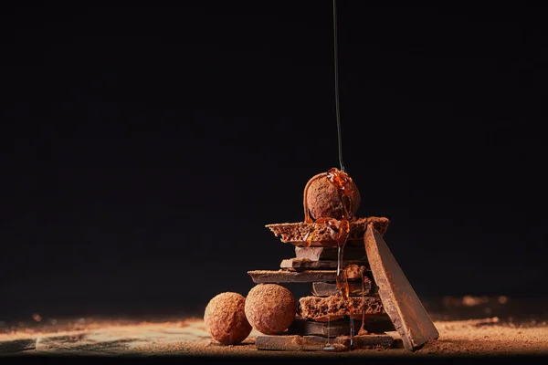 Vista da vicino del processo di versamento del caramello su tartufi e barrette di cioccolato con processo di cacao in polvere sul nero — Foto stock