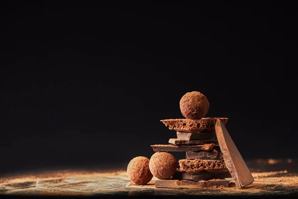 Close up view of arrangement of truffles and chocolate bars with cocoa powder on black — Stock Photo