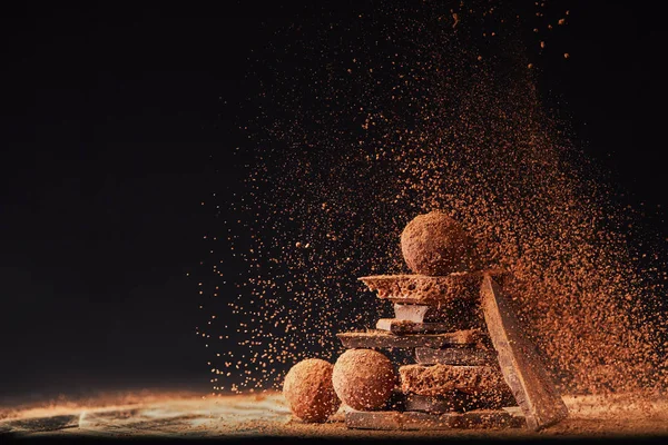 Vue rapprochée de l'arrangement des truffes et des barres de chocolat avec de la poudre de cacao sur noir — Photo de stock