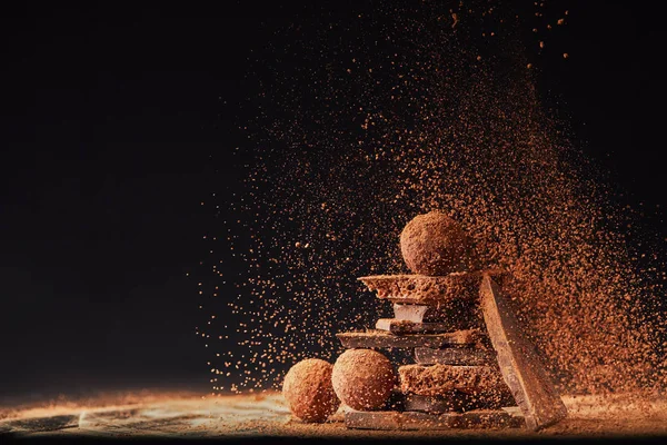 Close up view of arrangement of truffles and chocolate bars with cocoa powder on black — Stock Photo