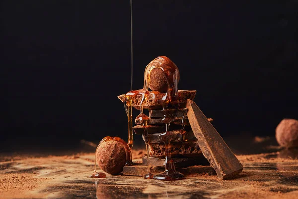 Vista da vicino del processo di versamento del caramello su tartufi e barrette di cioccolato con processo di cacao in polvere sul nero — Foto stock