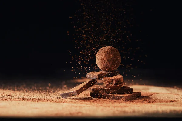 Close up view of truffle on chocolate bars with cocoa powder on black — Stock Photo