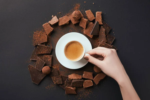 Tiro recortado da mão feminina, xícara de café, trufas e chocolate na superfície cinza — Fotografia de Stock