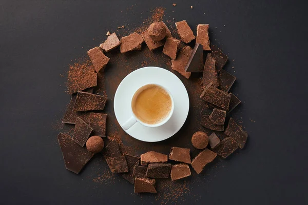 Vista dall'alto di una tazza di caffè, tartufi e barrette di cioccolato con cacao in polvere su un tavolo grigio — Foto stock