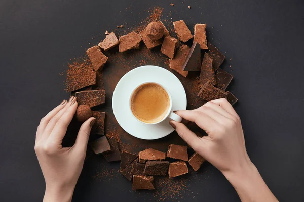 Tiro recortado de mãos femininas, xícara de café, trufas e chocolate na superfície cinza — Fotografia de Stock