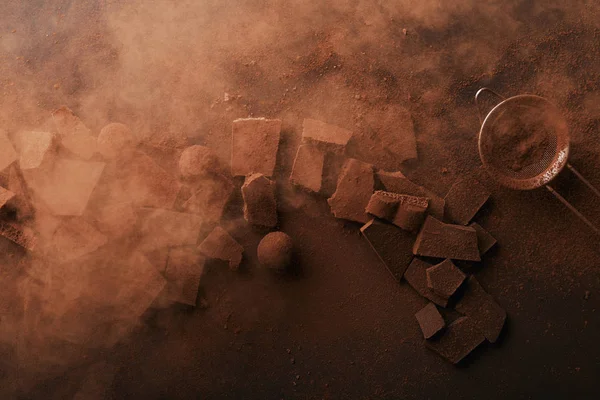 Vista superior de arranjo de vários tipos de chocolate, trufas e peneira com cacau em pó — Fotografia de Stock