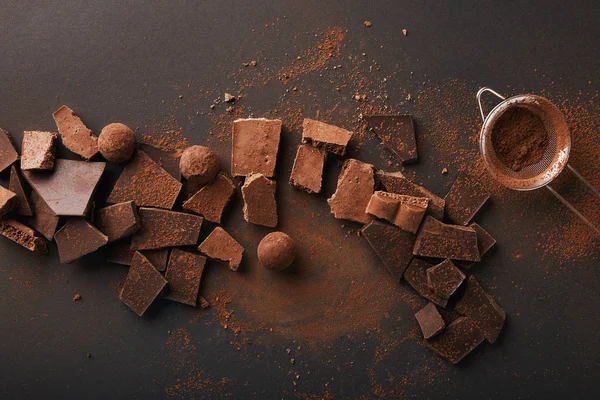 Vista superior de arranjo de vários tipos de chocolate, trufas e peneira com cacau em pó — Fotografia de Stock