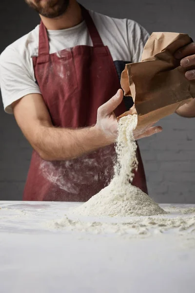 Imagen recortada de chef vertiendo harina en la mesa - foto de stock