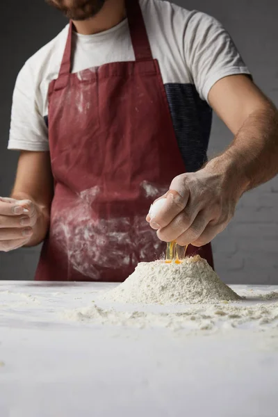 Imagen recortada de chef preparando masa y añadiendo huevo a la harina - foto de stock