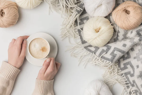 Cropped view of woman holding cup of coffee and yarn balls on blaket on white background — Stock Photo
