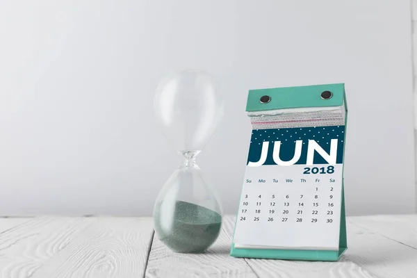 Vista de cerca del reloj de arena y el calendario de junio en la mesa de madera aislado en blanco - foto de stock