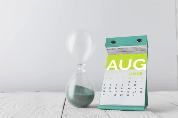 Vue rapprochée du sablier et du calendrier d'août sur plateau en bois isolé sur fond blanc — Photo de stock