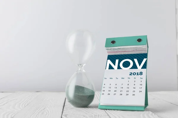 Close up view of hourglass and november calendar on wooden tabletop isolated on white — Stock Photo