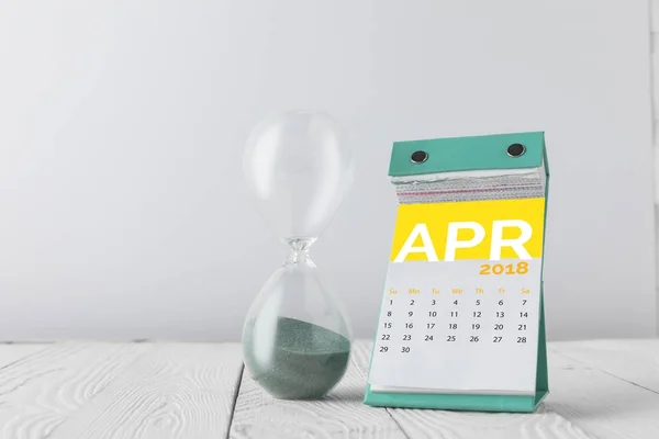 Vista de cerca del reloj de arena y el calendario de abril en la mesa de madera aislado en blanco - foto de stock