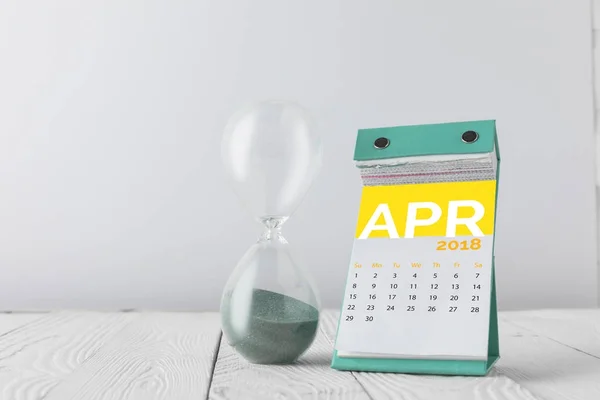 Vista de perto de ampulheta e calendário de abril em mesa de madeira isolada em branco — Fotografia de Stock