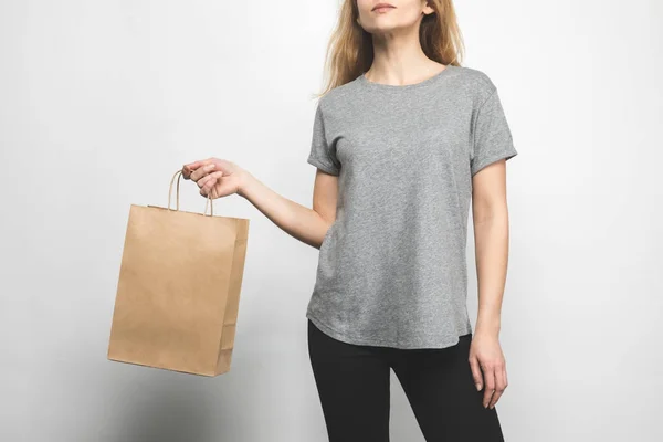 Cropped shot of woman in blank grey t-shirt on white with shopping bag — Stock Photo