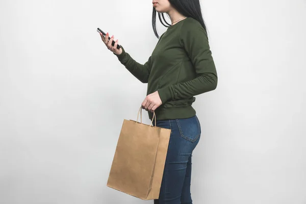 Mujer joven en sudadera verde en blanco con bolsa de compras - foto de stock