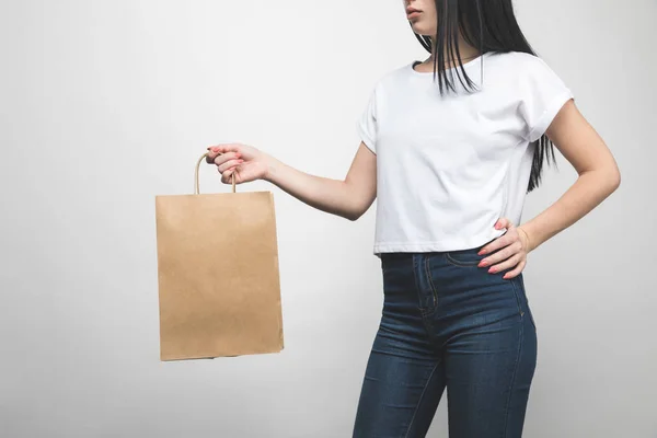 Cropped shot of young woman in blank t-shirt on white with shopping bag — Stock Photo