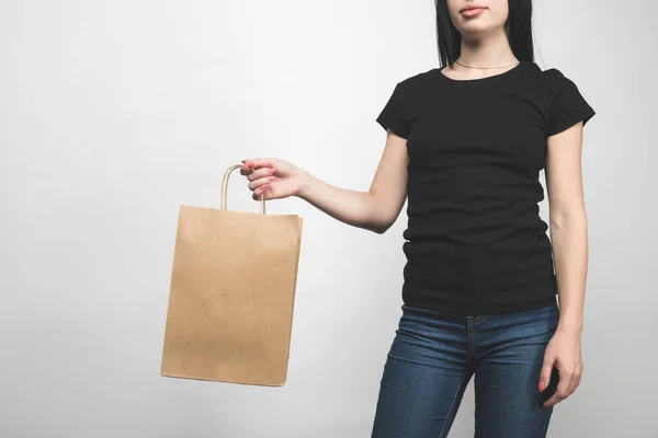 Cropped shot of young woman in blank black t-shirt isolated on white with shopping bag — Stock Photo