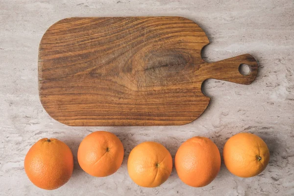 Vista superior de la fila de naranjas y tabla de cortar en la mesa de mármol - foto de stock