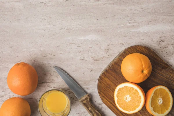 Вид сверху на апельсины, нож и деревянную доску на мраморной поверхности — стоковое фото