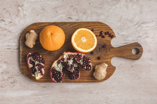 Vue de dessus des oranges, grenade et gingembre sur planche à découper — Photo de stock