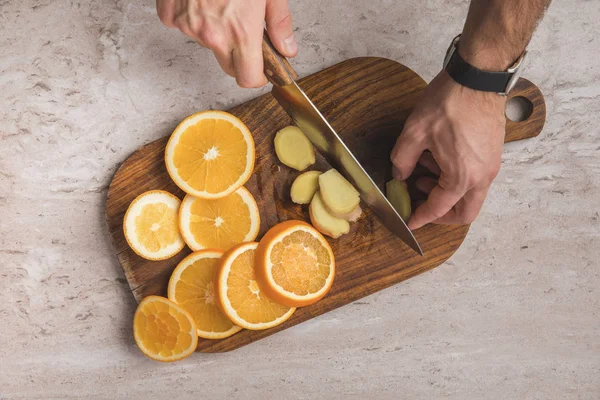 Cropped image of man cutting ginger on wooden board — Stock Photo