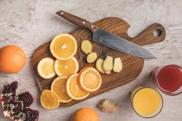 Вид сверху на срезанные апельсины, имбирь и гранат с домашними соками на столе — стоковое фото