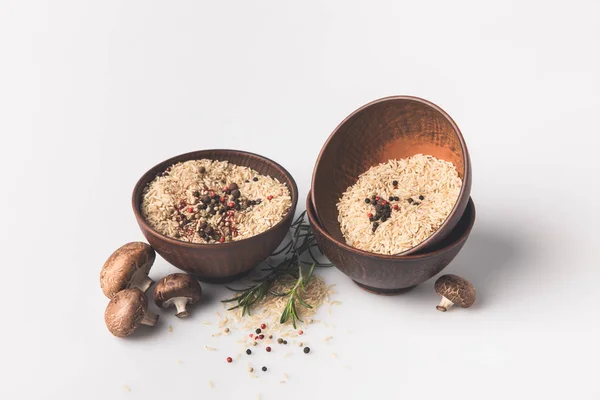 Tazones de arroz crudo con especias y champiñones en la superficie blanca - foto de stock