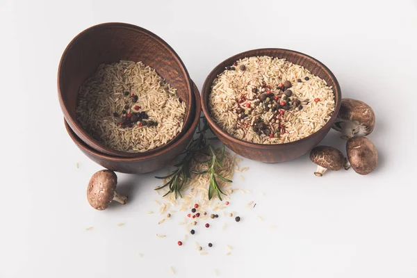 Schalen mit rohem Reis mit Gewürzen und Pilzen auf weißer Tischplatte — Stockfoto