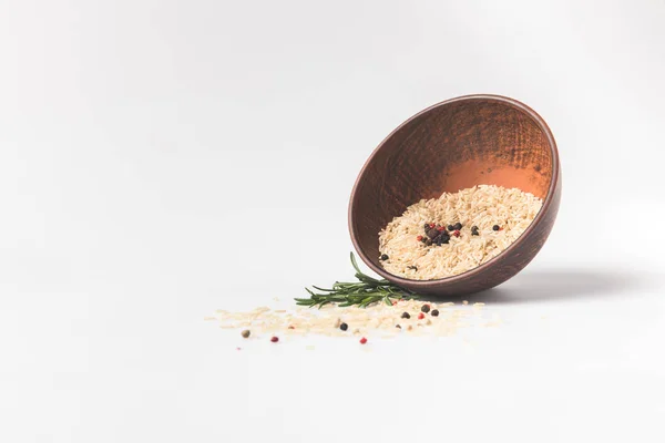 Raw rice and spices spilling out bowl on white surface — Stock Photo