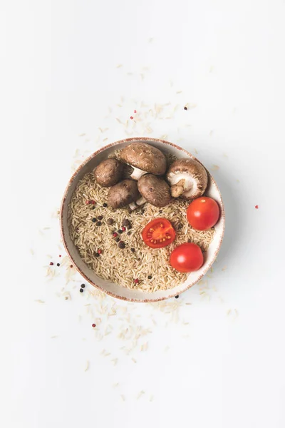 Roher Reis in Schüssel mit Pilzen und Tomaten auf weißer Oberfläche mit verschüttetem Reis und Gewürzen — Stockfoto