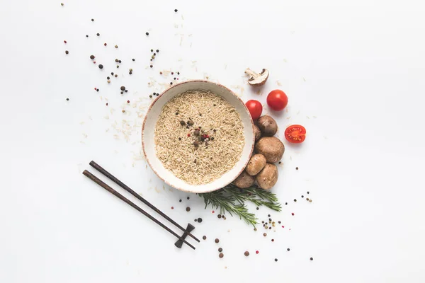 Flat lay composition of raw rice in bowl with mushrooms and tomatoes on white surface with chopsticks — Stock Photo