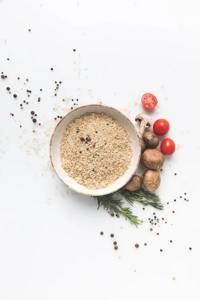 Flat lay composition of raw rice in bowl with mushrooms and tomatoes on white surface — Stock Photo
