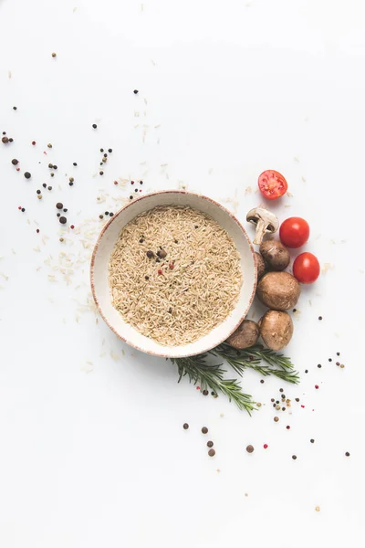 Composición plana de arroz crudo en tazón con champiñones y tomates en la superficie blanca - foto de stock