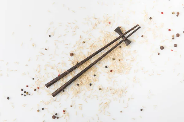 Top view of raw rice and spices spilled on white surface with chopsticks — Stock Photo