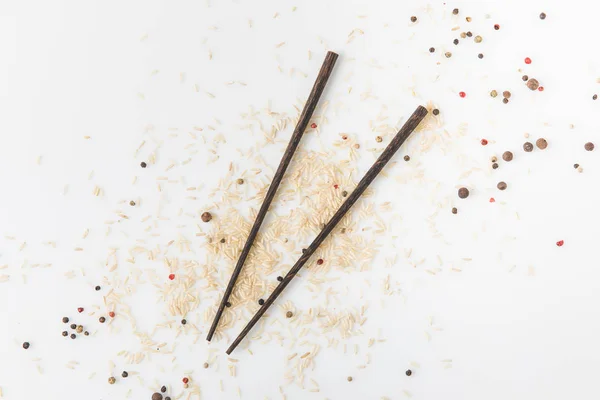 Vue de dessus du riz cru et des épices répandues sur la surface blanche avec des baguettes — Photo de stock