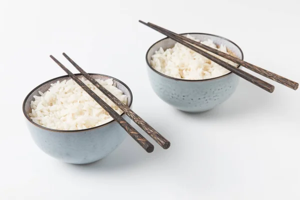 Миски вкусного риса с палочками на белой поверхности — стоковое фото