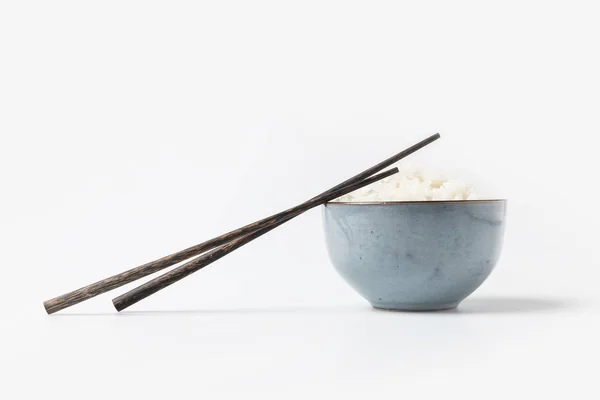 Bol de riz savoureux avec des baguettes sur la table blanche — Photo de stock