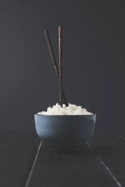 Bowl of freshly cooked rice with chopsticks on black table — Stock Photo