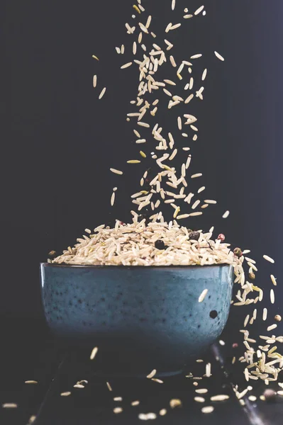 Close-up shot of rice spilling into bowl on black table — Stock Photo